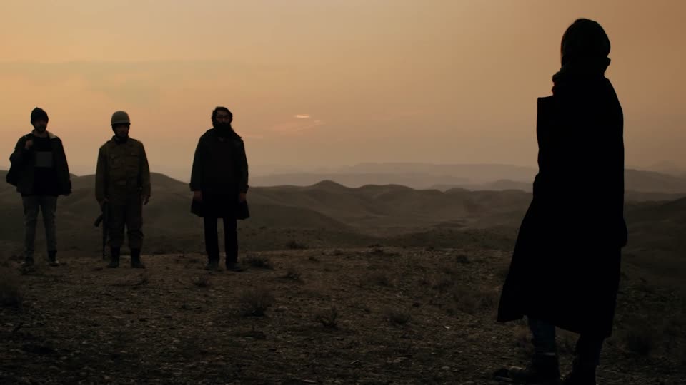 Silhouetted figures and a soldier on a desert ridge at dusk