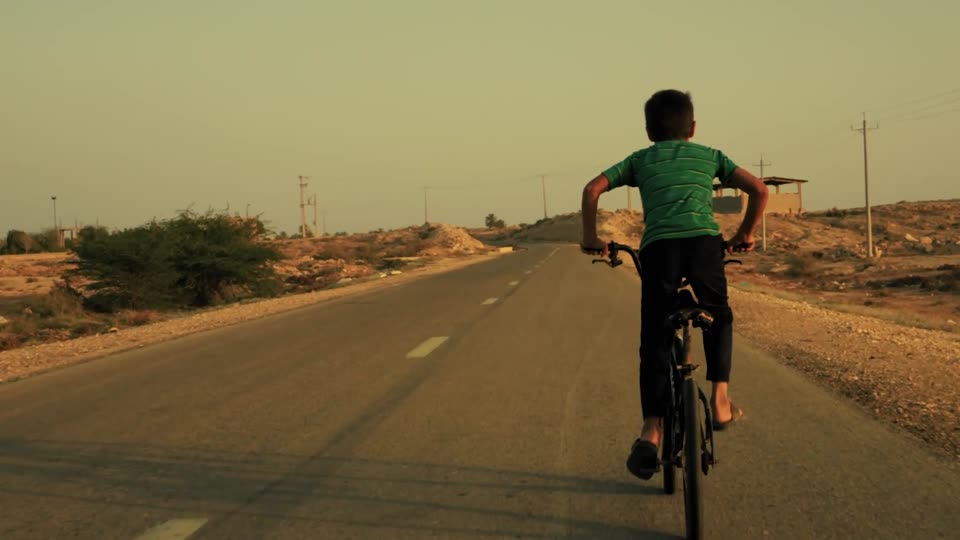 A boy in a green shirt cycles down an empty desert road
